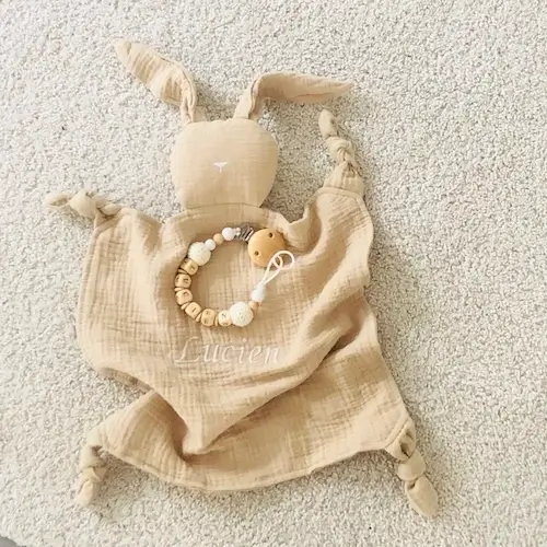 Coffret naissance doudou attache-tétine beige personnalisé : Un cadeau unique alliant douceur et praticité, avec un doudou en gaze de coton et une attache-tétine en bois naturel faits main pour accompagner bébé en toute sécurité.